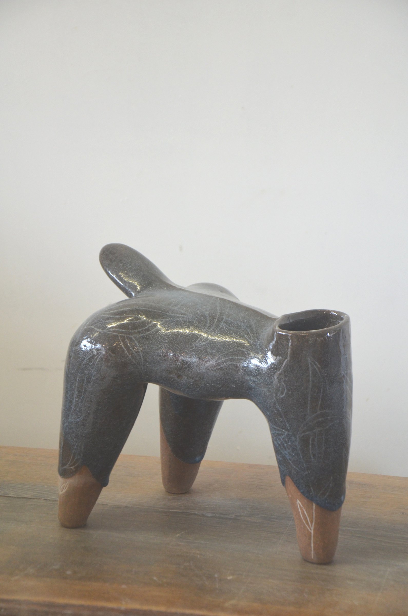 Pièce à quatre pieds couverte d'un émail gris brillant, les pieds laissés en terre nue, sur une table en bois.