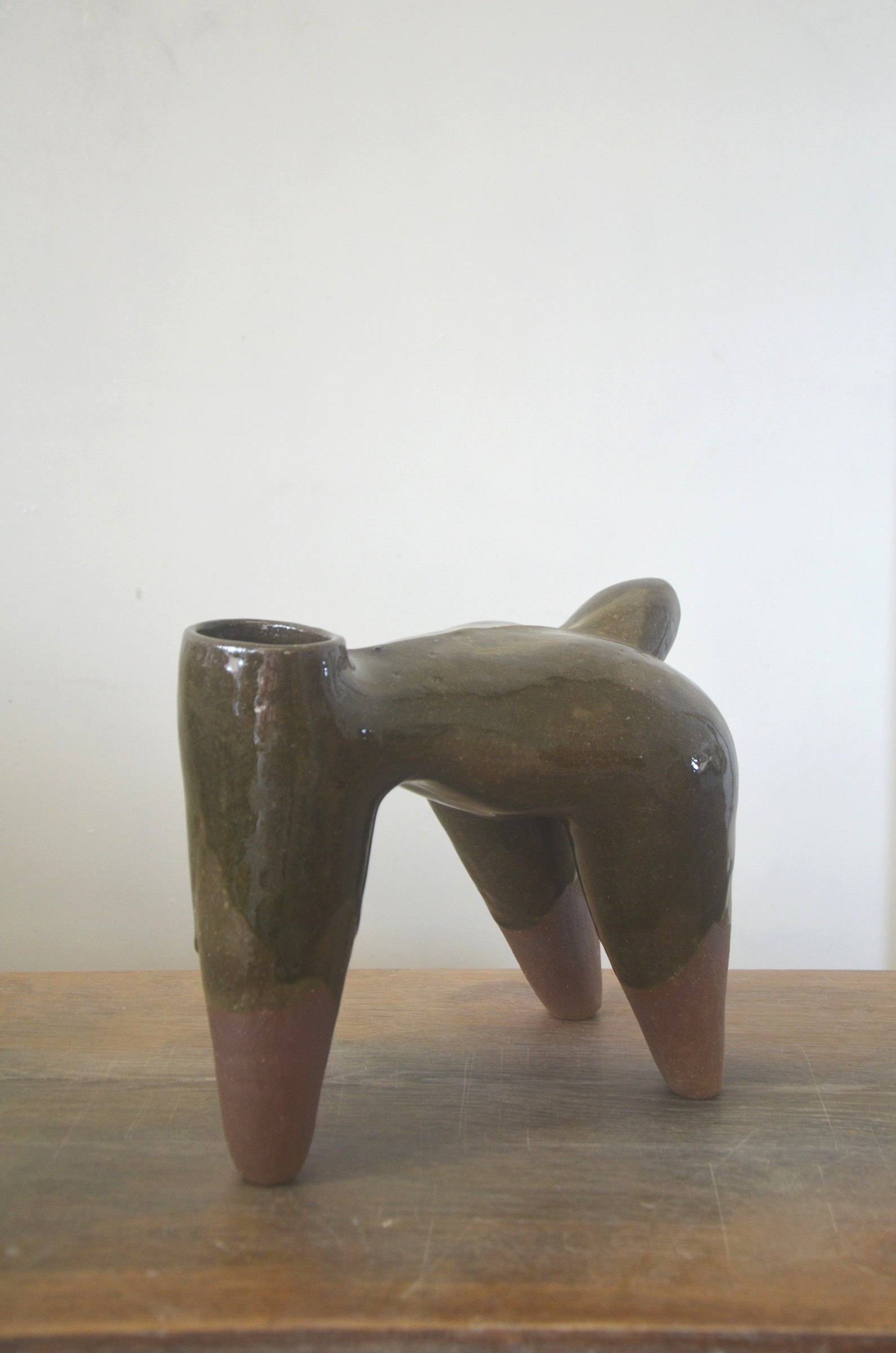 Pièce à quatre pieds couverte d'un émail vert-brun coulant, les pieds laissés en terre nue, sur une table en bois.